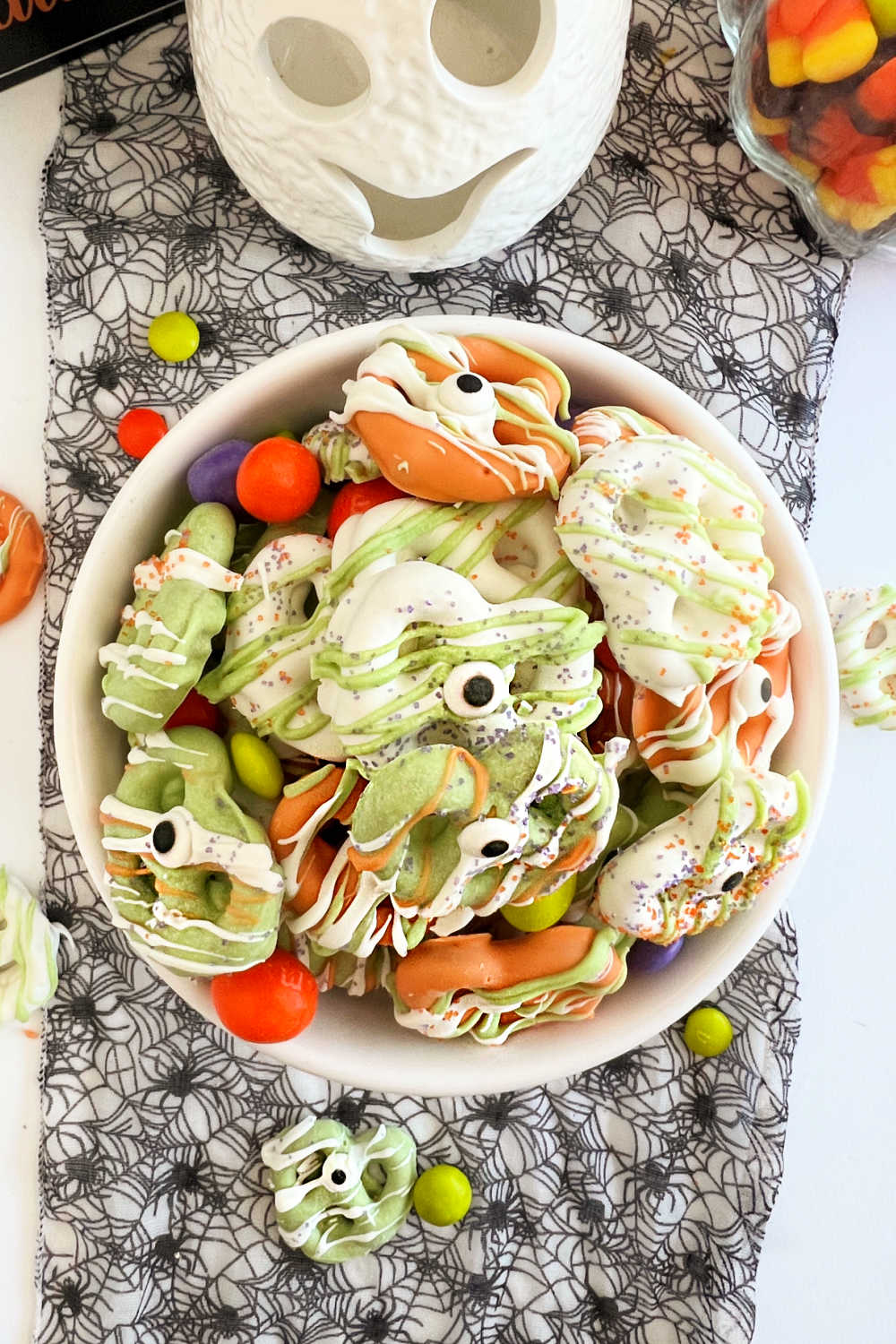 green, white and orange halloween pretzels with candy eyes in bowl