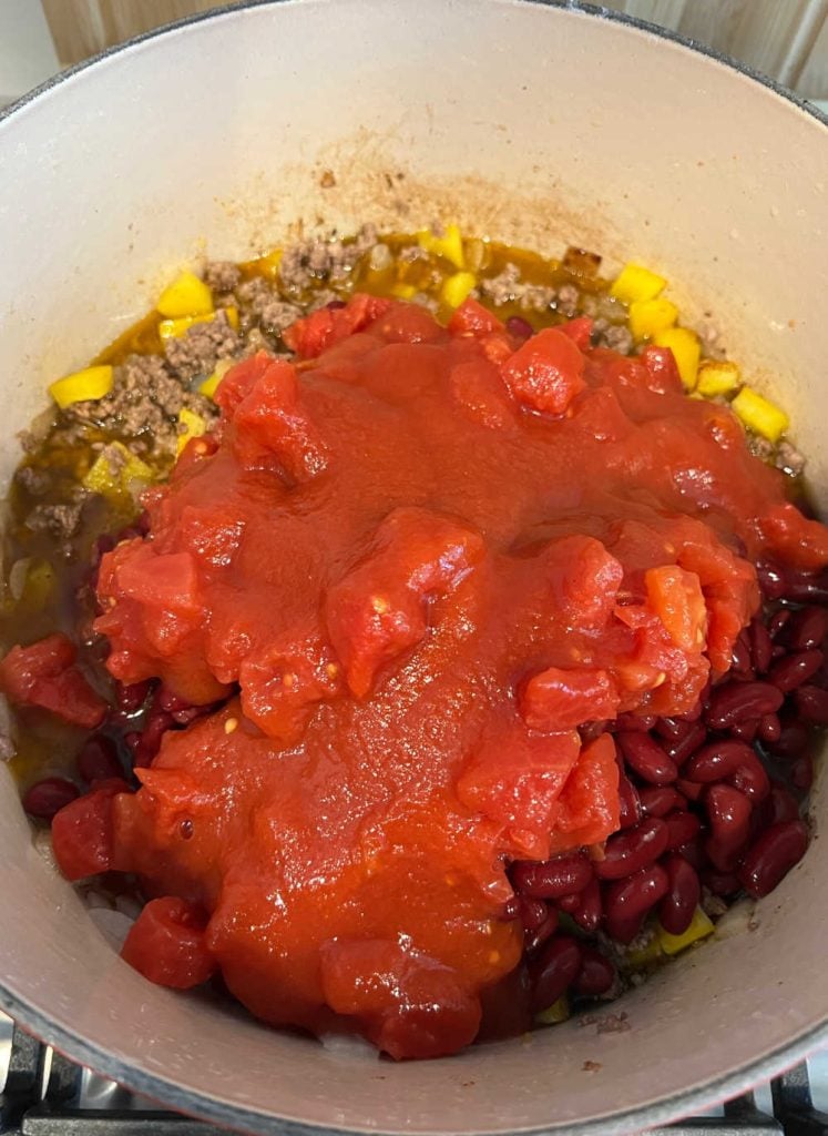 ground beef, peppers, kidney beans and tomatoes in dutch oven on stovetop