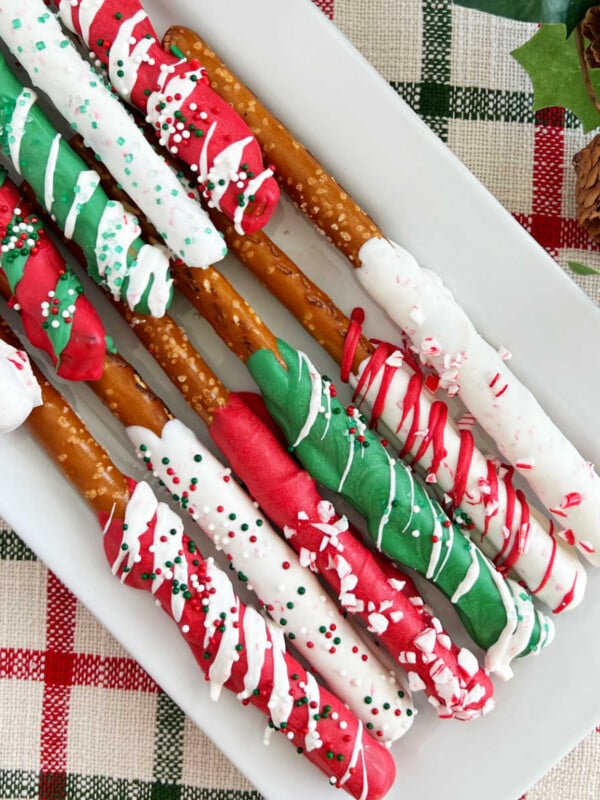 chocolate covered Christmas pretzel rods with sprinkles on white platter