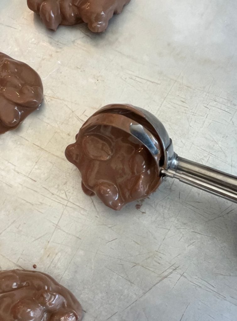 place melted chocolate peanut clusters on cookie sheet with cookie scoop