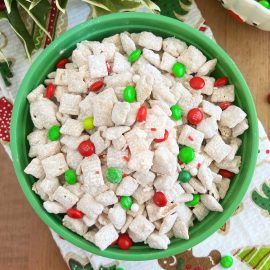 white chocolate puppy chow with sprinkles and Christmas m and m candies in a green bowl