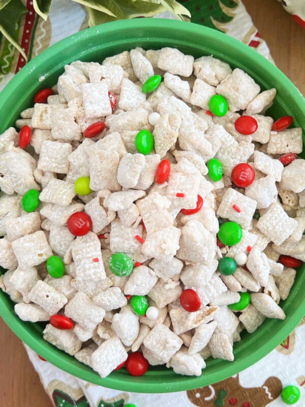 white chocolate puppy chow with sprinkles and Christmas m and m candies in a green bowl