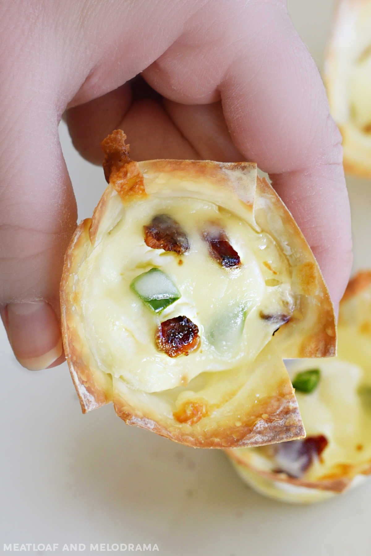 hand holding mini jalapeno popper wonton cup with bacon