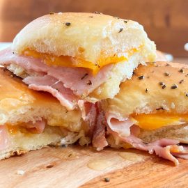 leftover ham sandwich made with spiral ham slices and cheddar cheese on buttery seasoned rolls on a serving board.