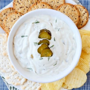 pickle dip with dill pickle slices and fresh dill in bowl with potato chips and crackers