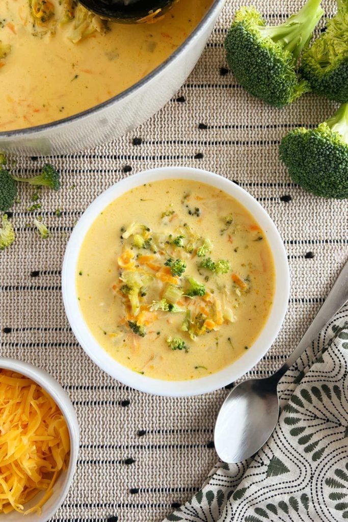 bowl of easy broccoli cheddar soup on the table with Dutch oven