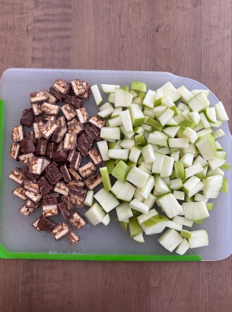 chopped snicker bars and green apples on cutting board