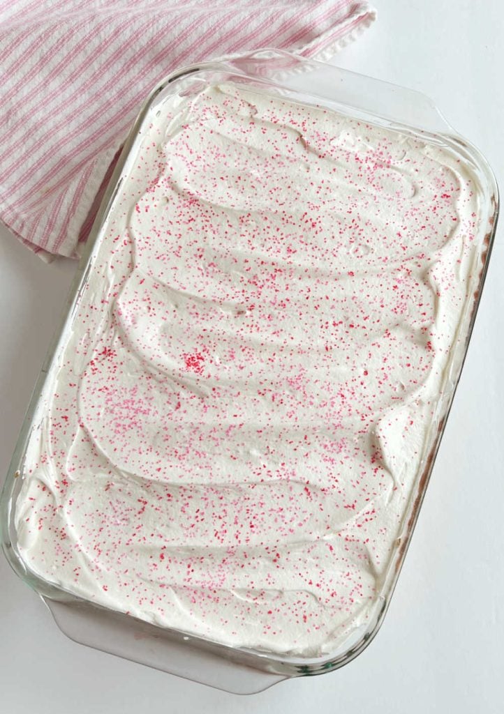 strawberry poke cake with cool whip frosting and sprinkles