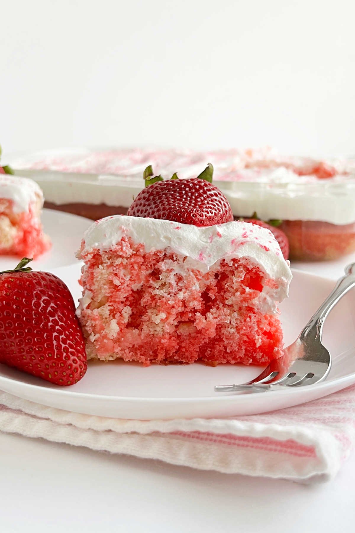 slice of strawberry jello poke cake with fresh strawberries on plate