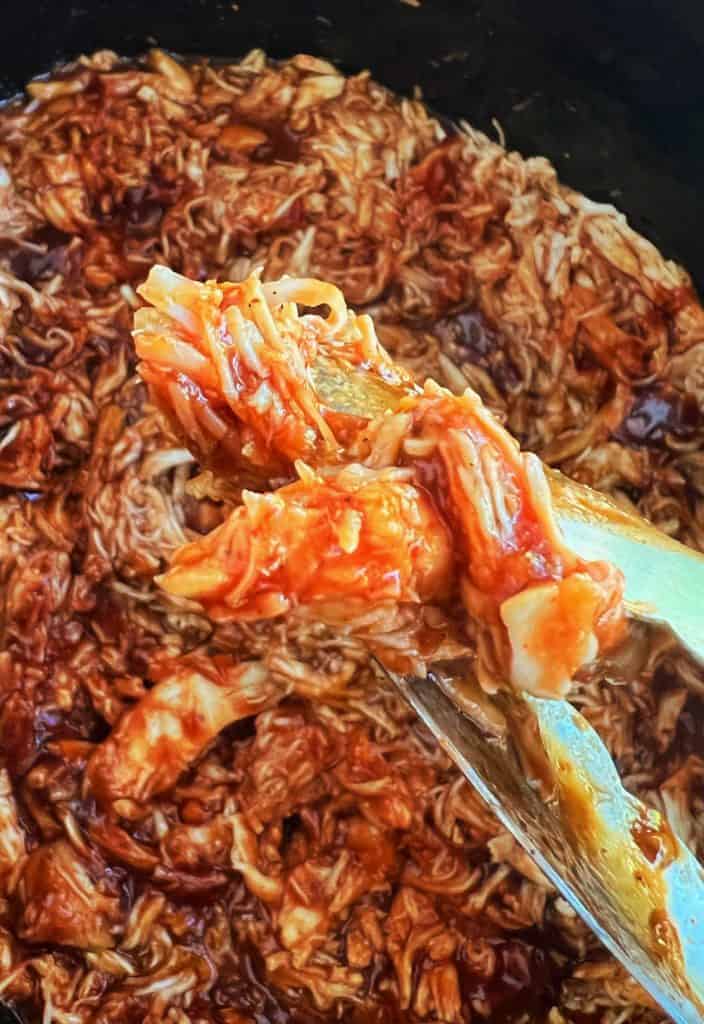 slow cooker bbq pulled chicken in kitchen tongs