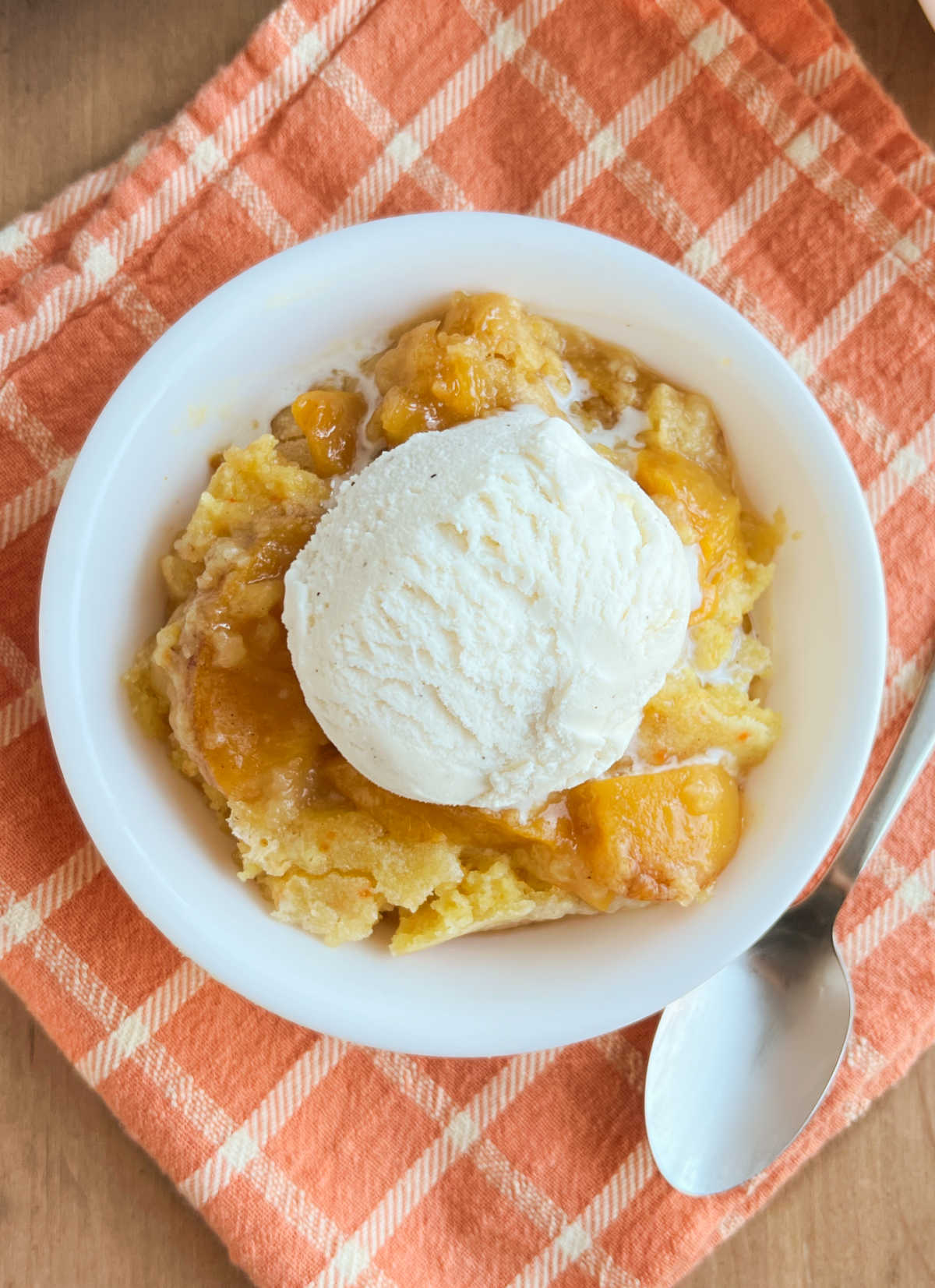 bowl of cake mix peach cobbler with vanilla ice cream on top