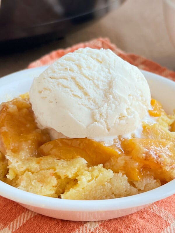 bowl of crock pot peach cobbler with a scoop of vanilla ice cream on top