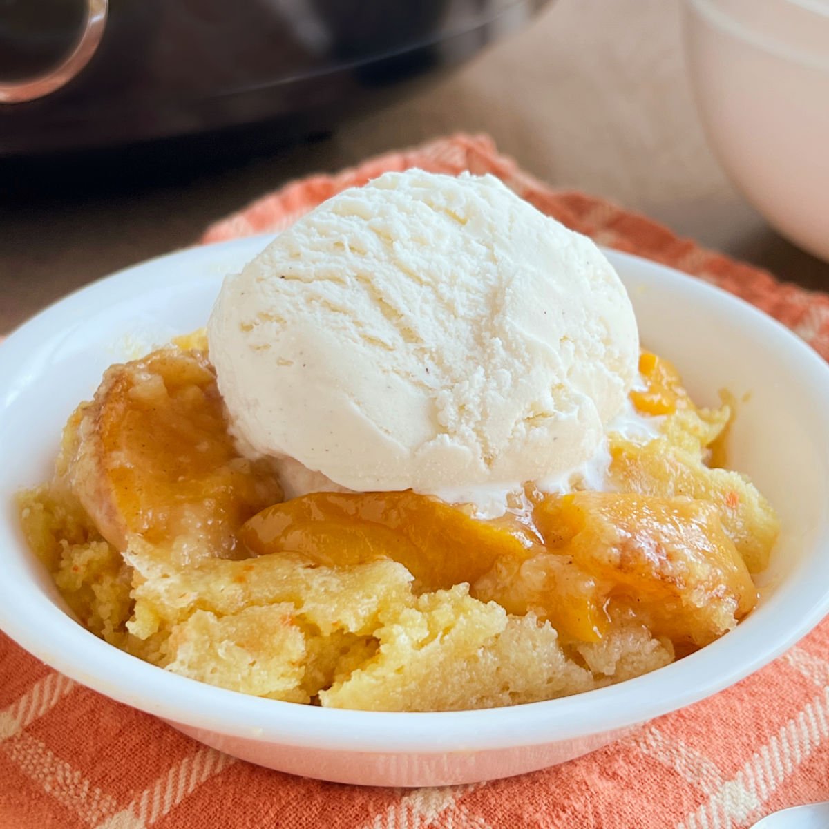 bowl of crock pot peach cobbler with a scoop of vanilla ice cream on top