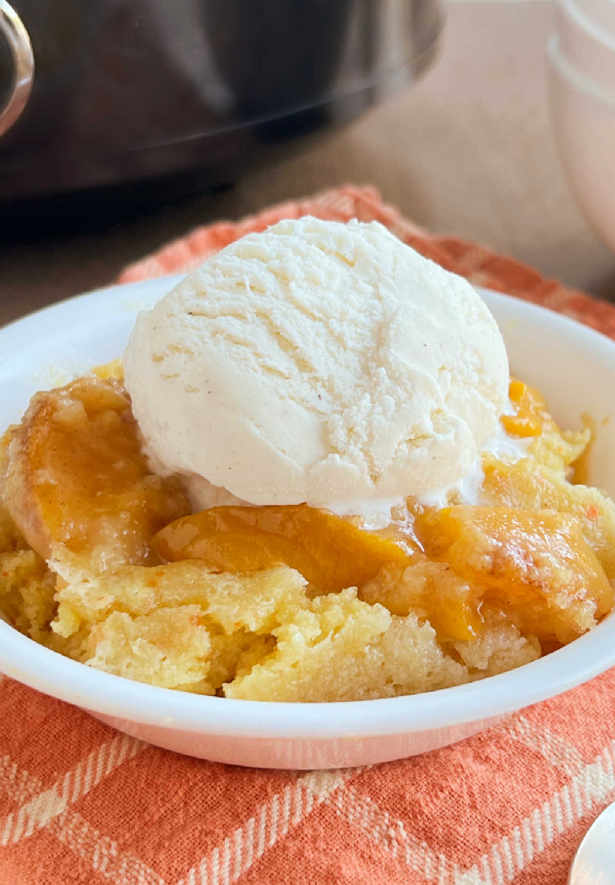 bowl of crock pot peach cobbler with a scoop of ice cream on top