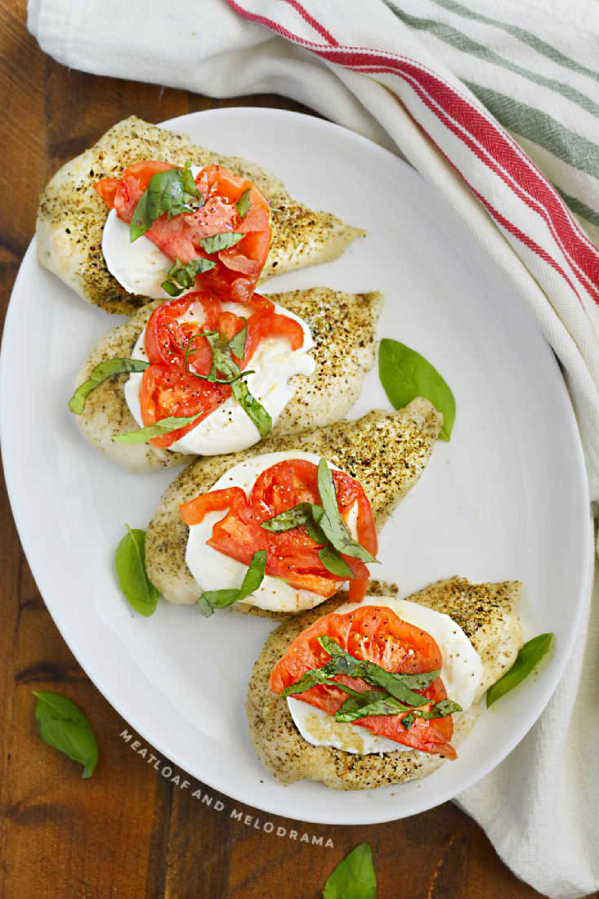 baked caprese chicken with mozzarella, tomatoes and fresh basil leaves on a platter