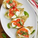 baked caprese chicken breasts with fresh mozzarella cheese, tomato slices and fresh basil leaves on a platter