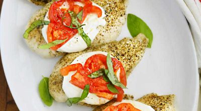 baked caprese chicken breasts with fresh mozzarella cheese, tomato slices and fresh basil leaves on a platter