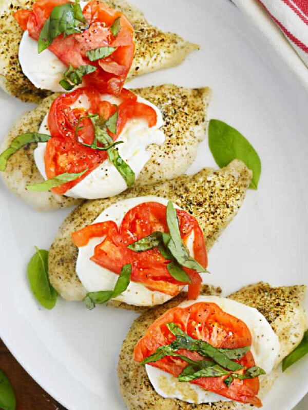 baked caprese chicken breasts with fresh mozzarella cheese, tomato slices and fresh basil leaves on a platter