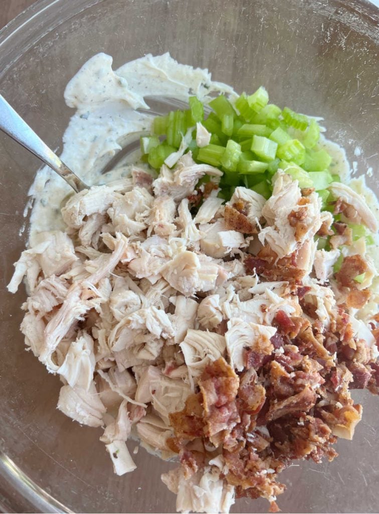 cooked chicken with chopped celery and bacon in ranch dressing in mixing bowl