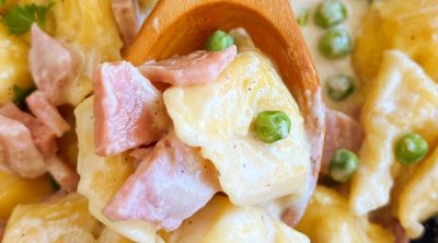 tortellini with ham and peas in creamy Parmesan cheese sauce on wooden spoon