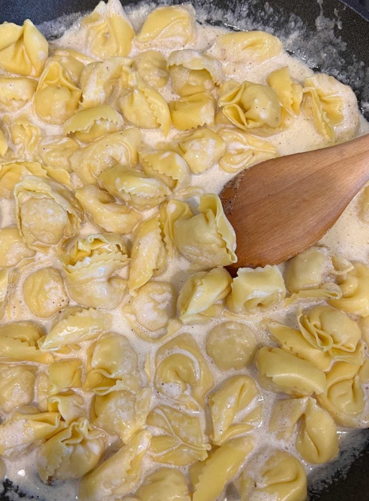 stir tortellini in cream sauce with wooden spoon