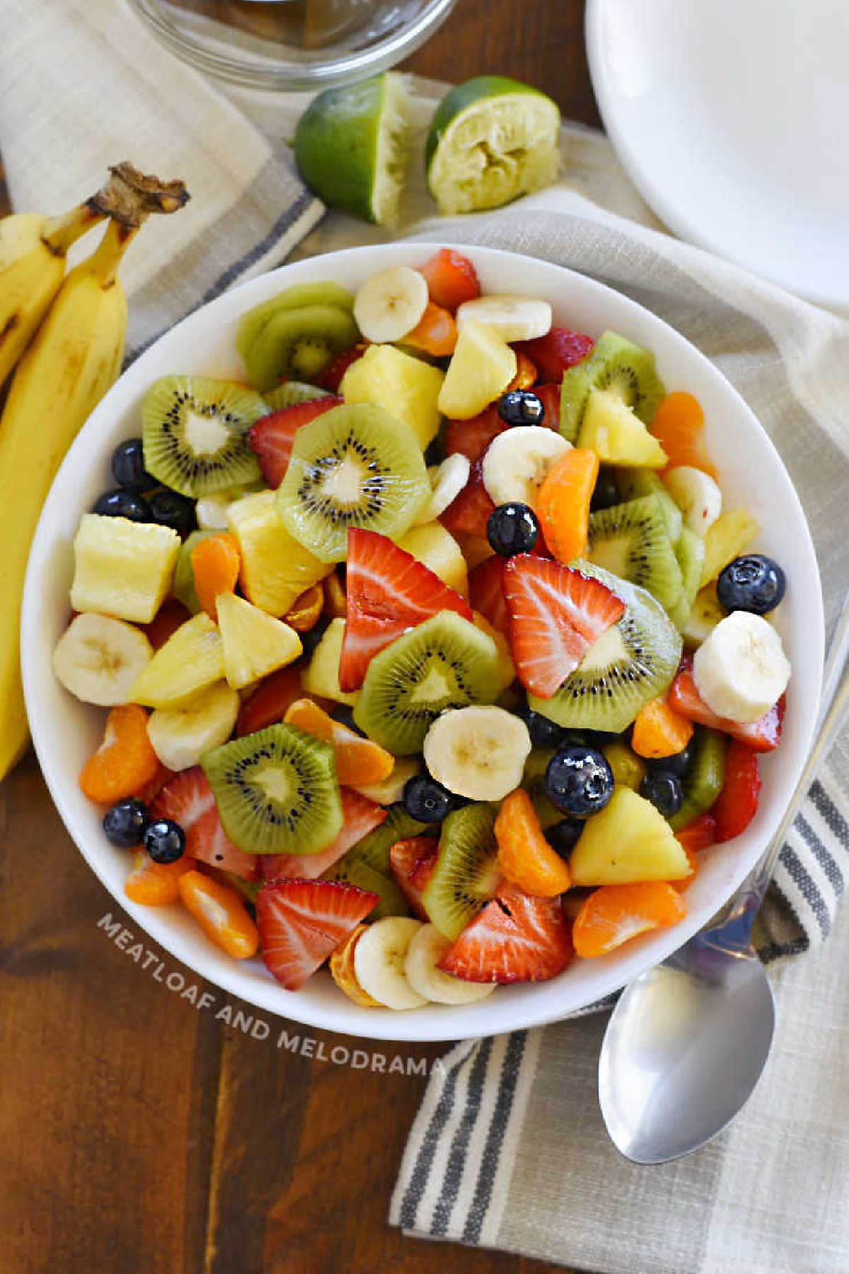 bowl of tropical fruit salad with mandarin oranges, kiwi, bananas, pineapple, strawberries, blueberries and honey lime dressing