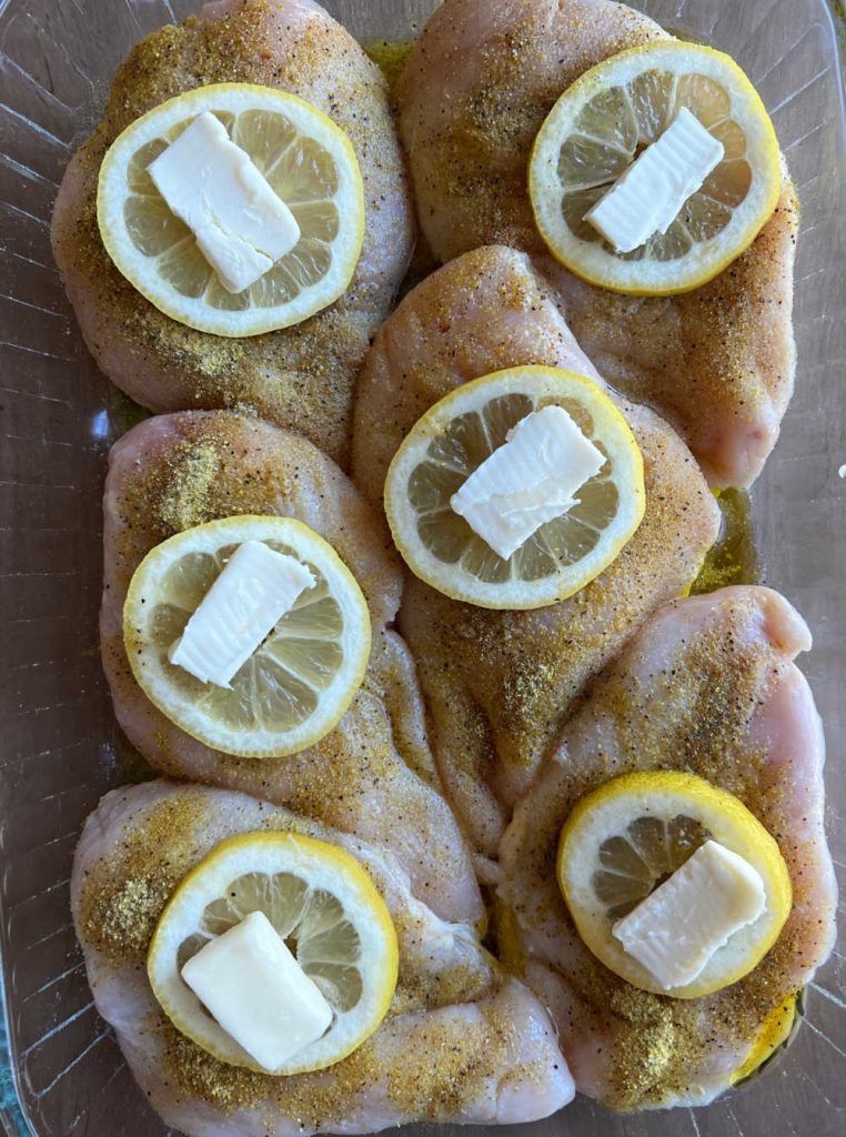 seasoned chicken topped with lemon slices and butter in baking dish