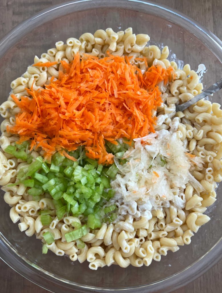 cooked macaroni pasta with shredded carrots, diced celery and grated onions in mixing bowl