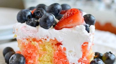 slice of red white and blue poke cake with strawberries and blueberries on a plate