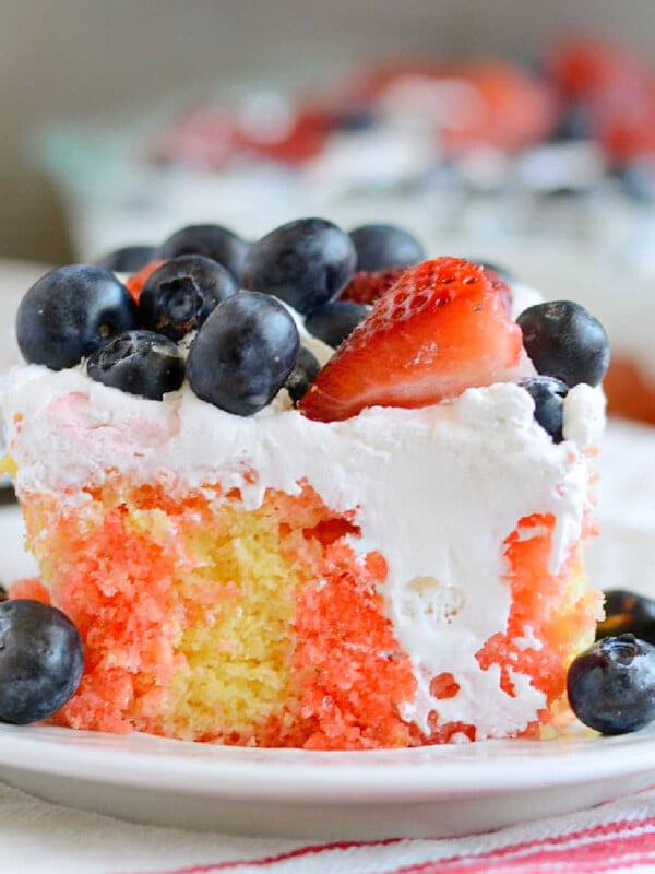 slice of red white and blue poke cake with strawberries and blueberries on a plate