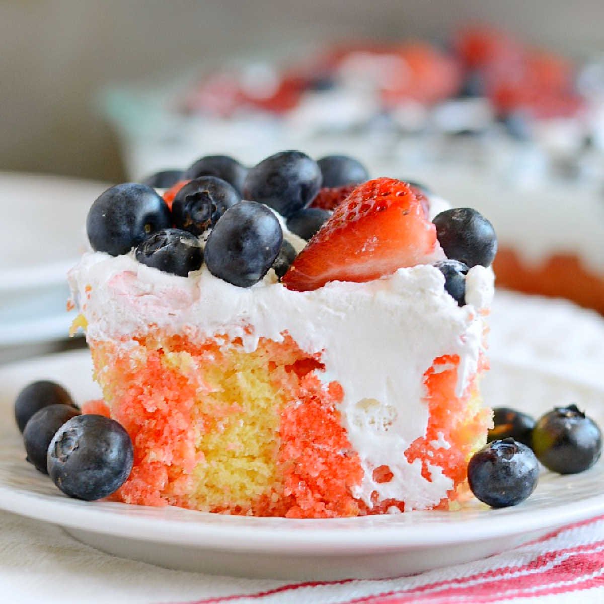 slice of red white and blue poke cake with strawberries and blueberries on a plate