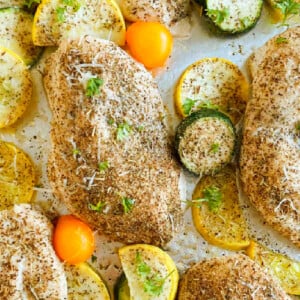 Baked chicken and zucchini with yellow squash and grape tomatoes on a sheet pan.