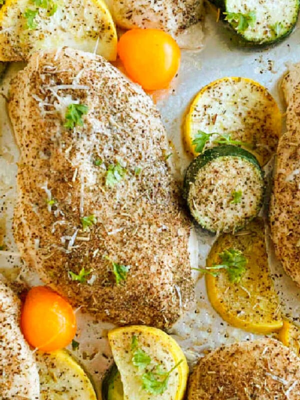 Baked chicken and zucchini with yellow squash and grape tomatoes on a sheet pan.