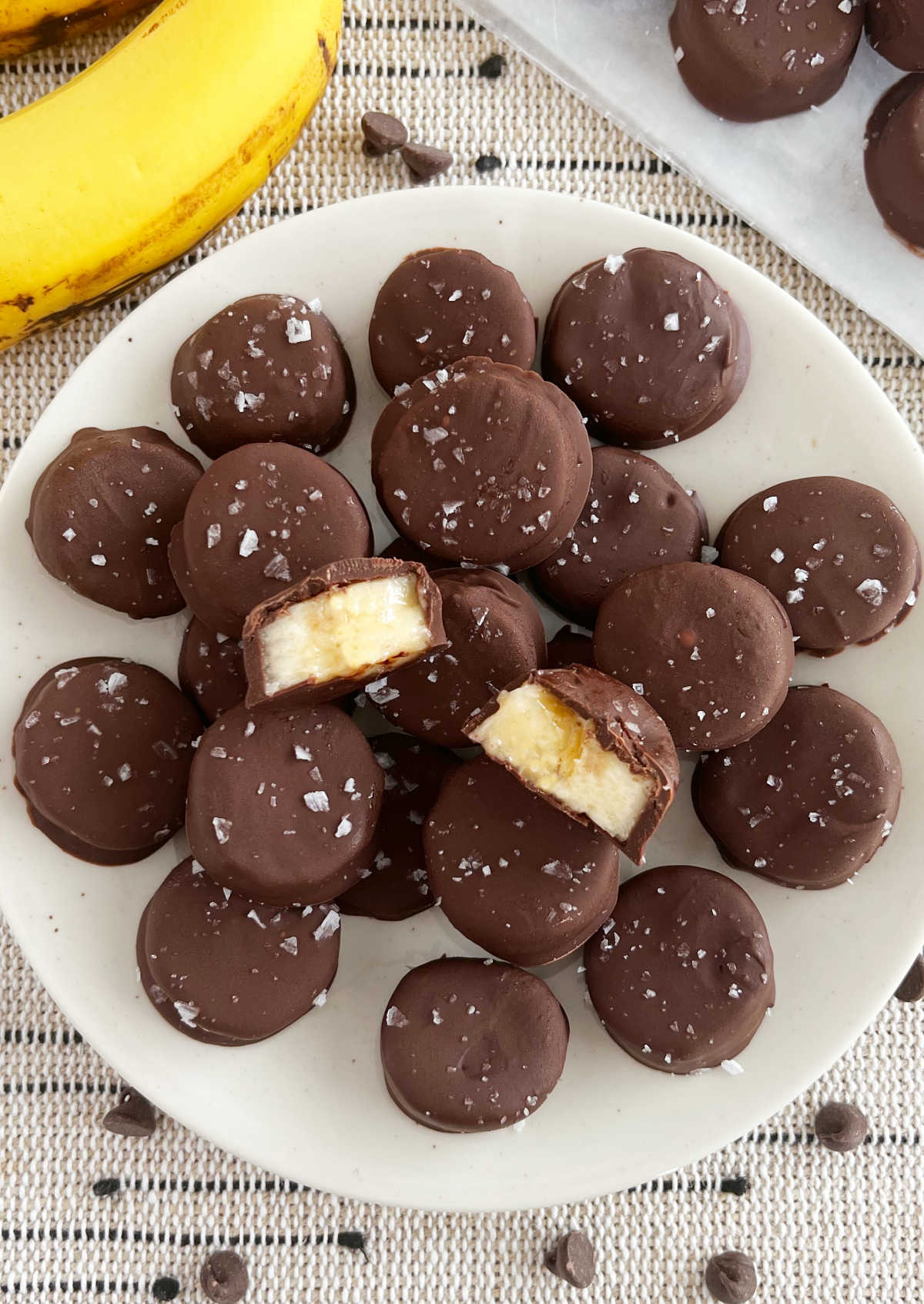 frozen chocolate covered banana bites with flaked salt stacked on a plate