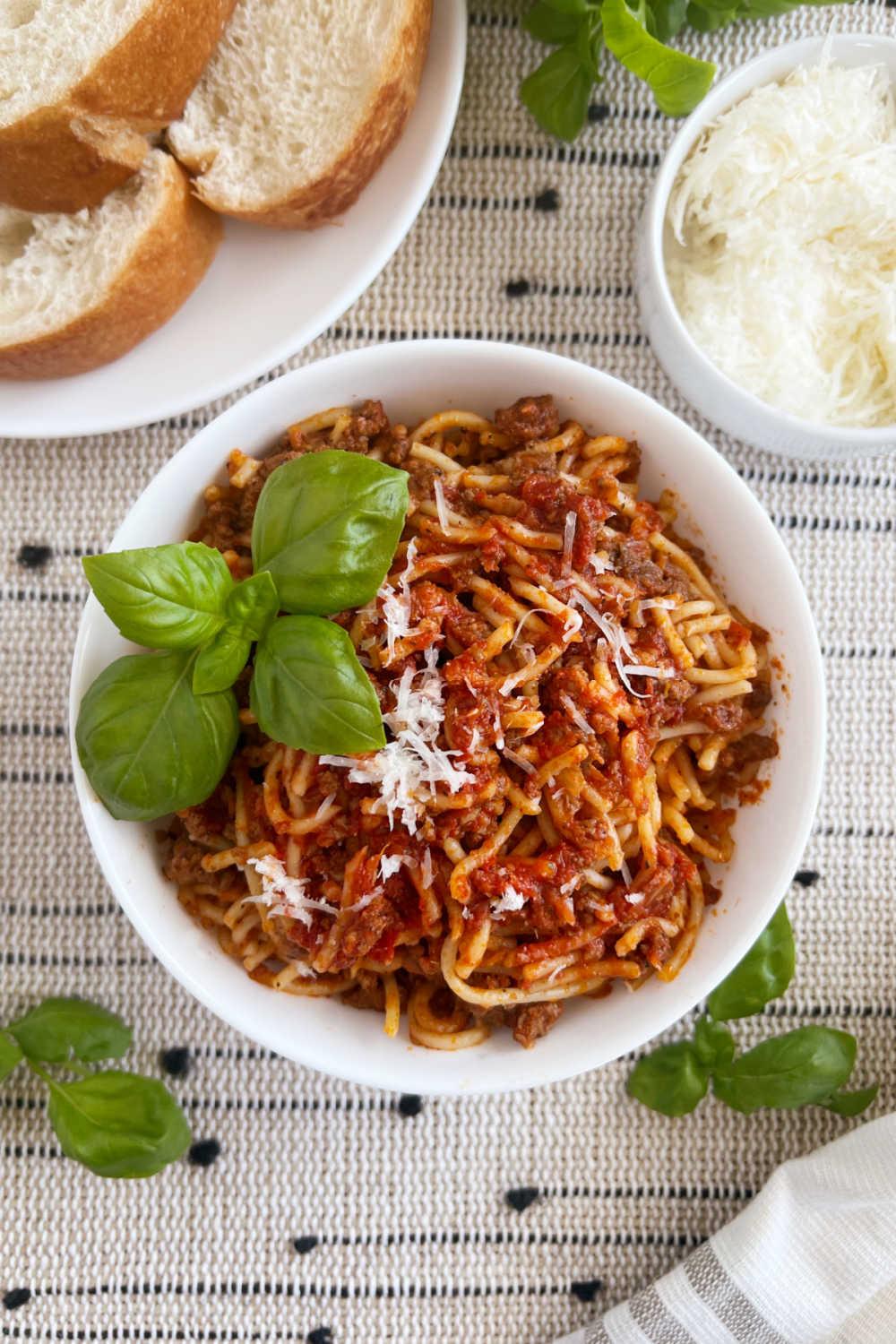 instant pot spaghetti and meat sauce in white bowl with basil, Parmesan cheese and bread