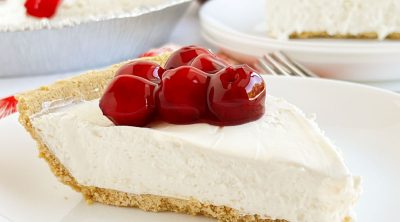 slice of no bake cheesecake with cool whip and cream cheese on graham cracker crust with cherry topping