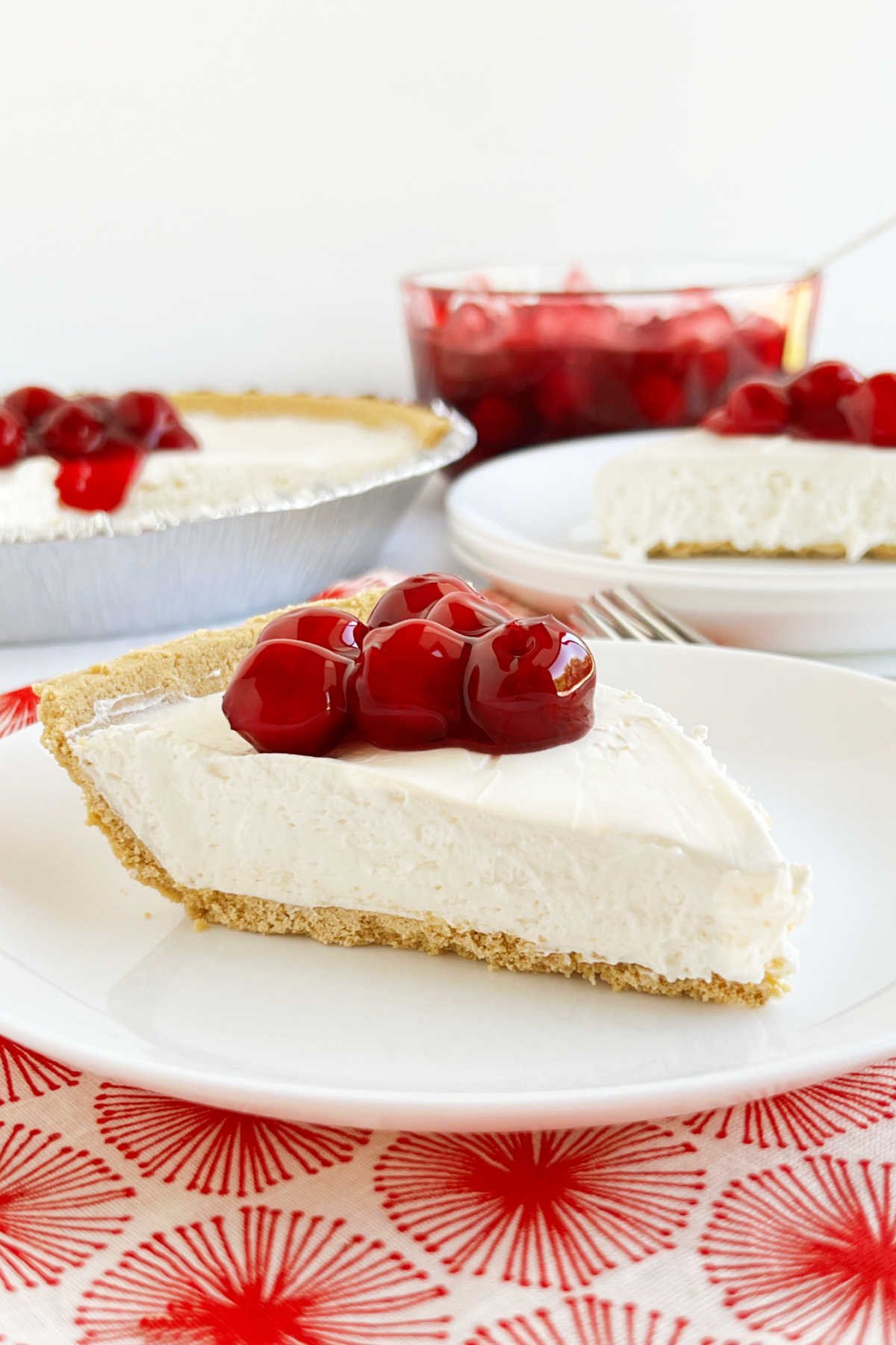 slice of no bake cheesecake with cool whip in graham cracker crust topped with cherry pie filling on plate