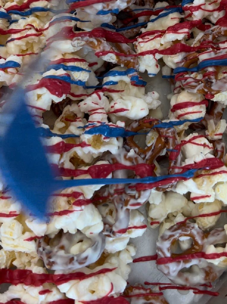 drizzle blue candy coating and red candy coating over popcorn mixture