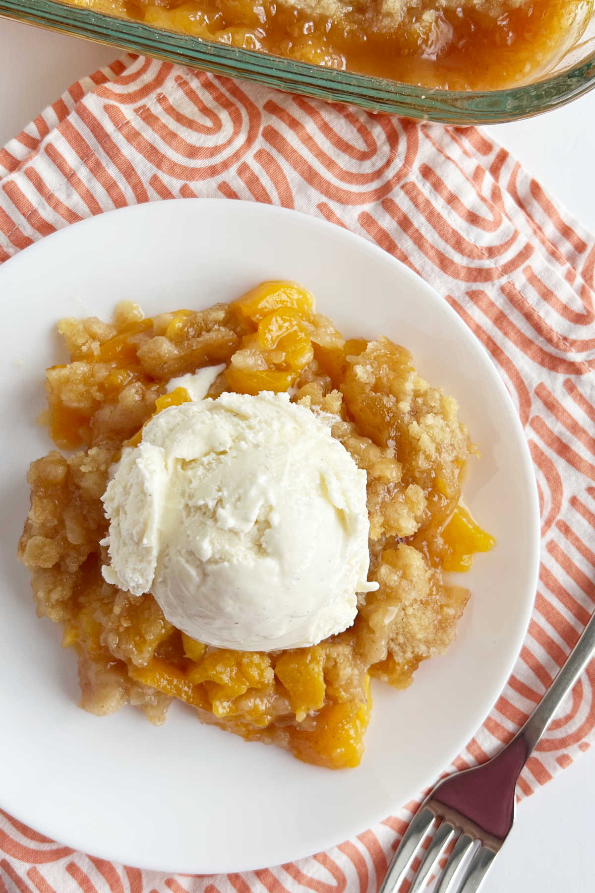 serving of peach crisp without oats topped with scoop of ice cream on plate
