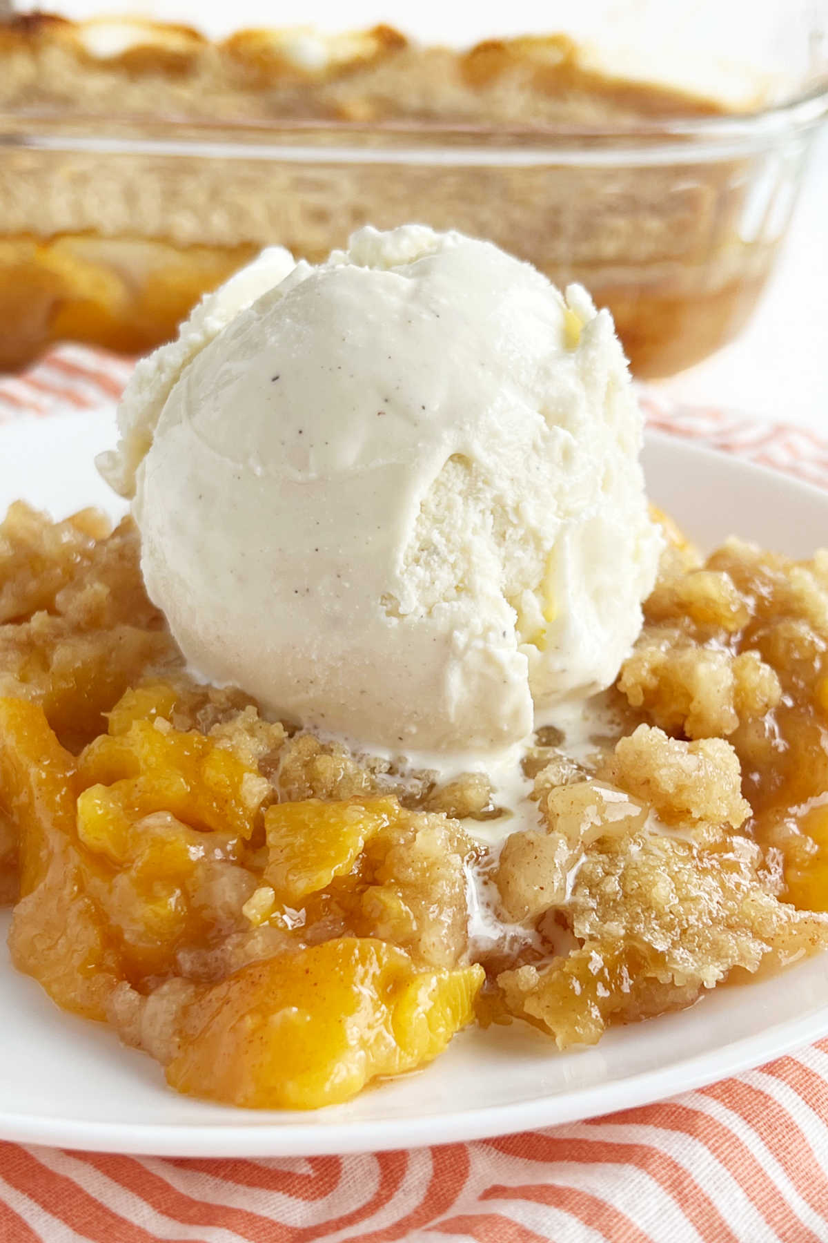 fresh peach crisp with scoop of vanilla ice cream on white plate