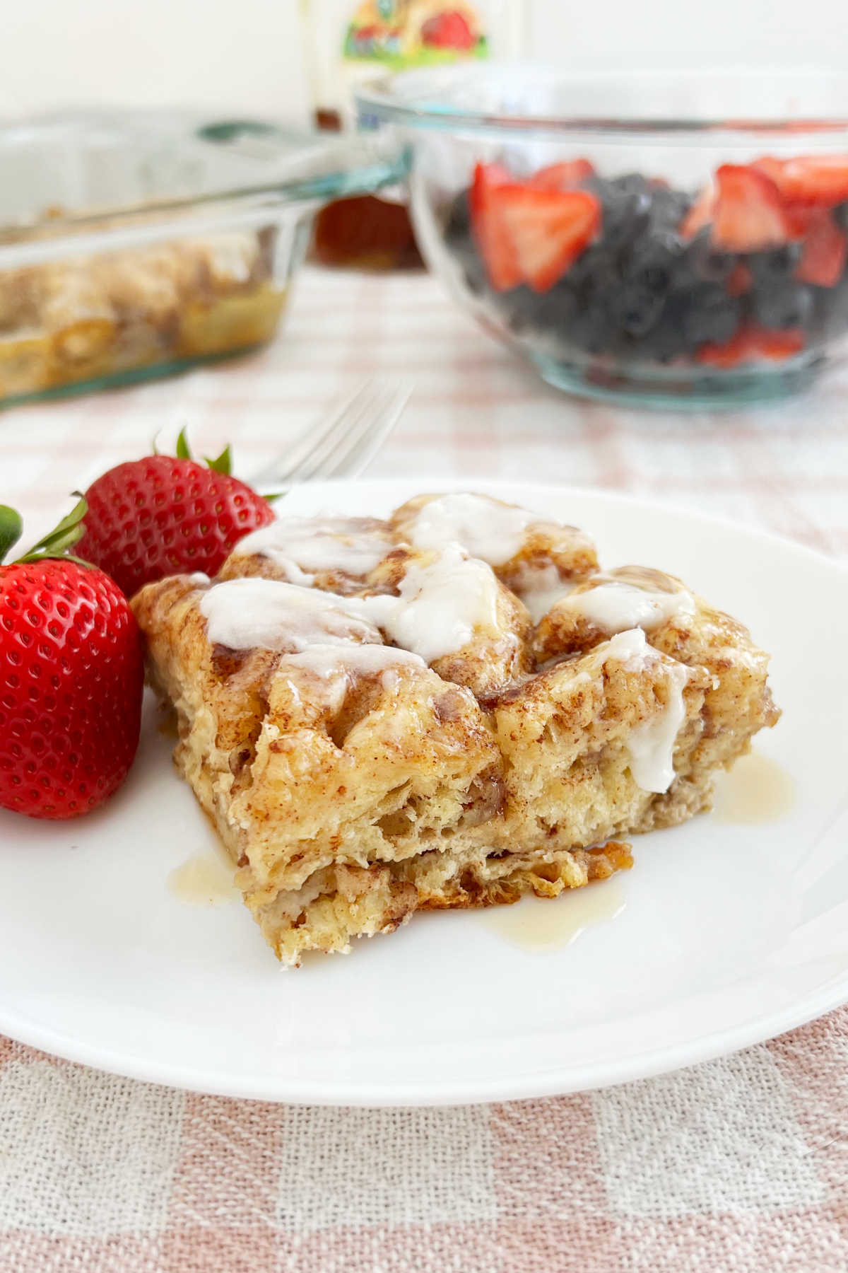 cinnamon roll casserole with frosting, strawberries and maple syrup on the table