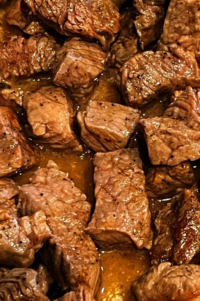 steak bites in garlic butter sauce in skillet.