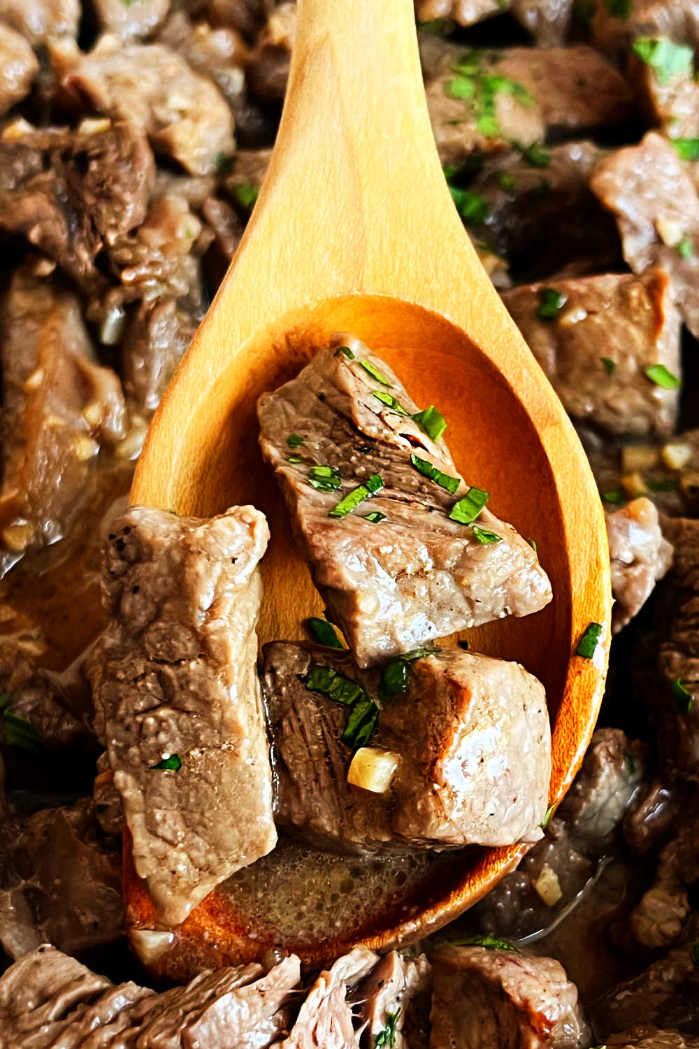 garlic butter steak bites with parsley on wooden serving spoon