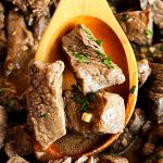 garlic butter steak bites with parsley in wooden spoon.
