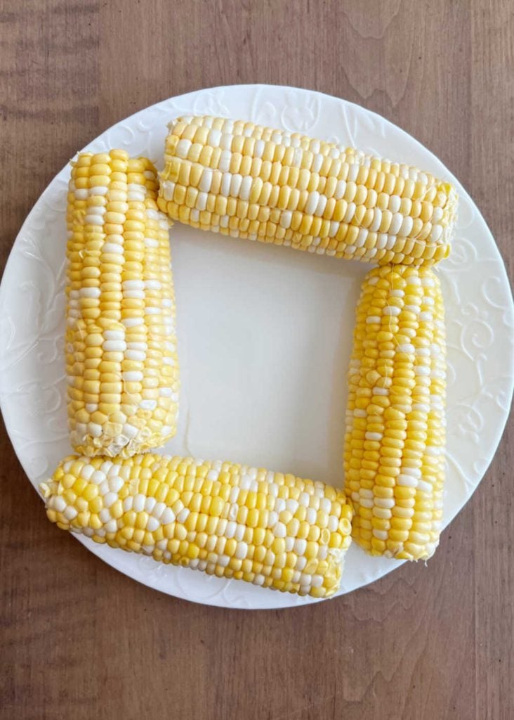 husked corn on cob on microwave-safe plate.