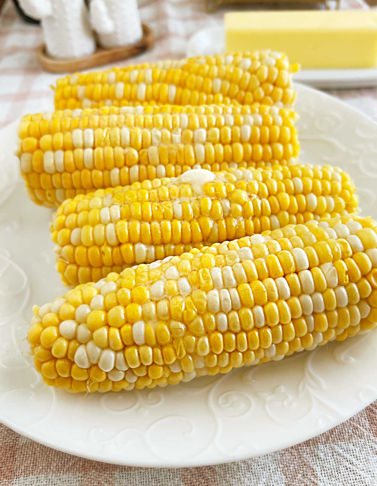 microwave corn on the cob with melted butter on white plate.