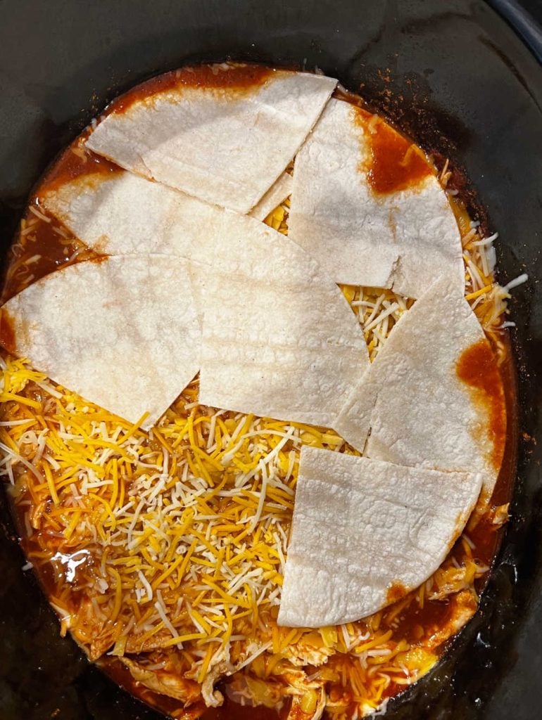 layer corn tortillas and cheese with shredded chicken and red sauce in crock pot.