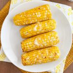 air fryer corn on the cob with butter on white plate.