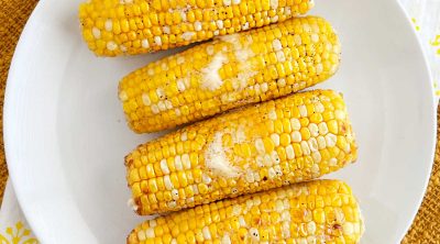 air fryer corn on the cob with butter on white plate.