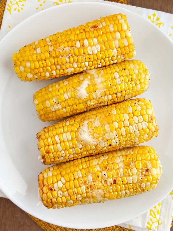 air fryer corn on the cob with butter on white plate.